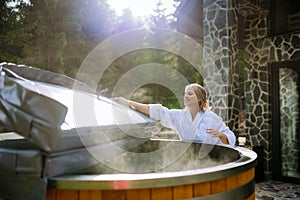 Woman in bathrobe opening lid of hot tub, checking temperature, ready for home spa procedure in hot tub outdoors