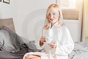 Woman in bathrobe relaxing in her bed in the morning with coffee