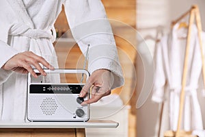 Woman in bathrobe turning volume knob on radio indoors, closeup. Space for text