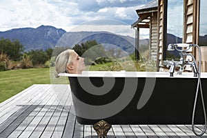 Woman In Bathtub On Porch Against Mountains