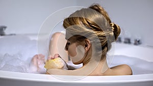 Woman in bathtub washing body, hygienic procedure, home spa concept, back view