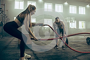 Woman with battle ropes exercise in the fitness gym.