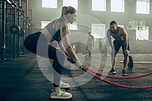 Woman with battle ropes exercise in the fitness gym.