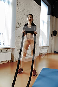 Woman with battle ropes exercise in the fitness gym.