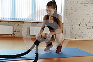 Woman with battle ropes exercise in the fitness gym.