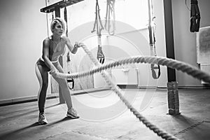 Woman with battle ropes exercise in the fitness gym. Young female wearing sportswear.