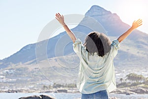 Woman at beach, arms in air and freedom, back view with mountains and travel, praise and sunshine. Female person outdoor