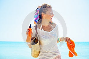 Woman with beach bag, orange flip flops and bottle of sunscreen