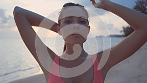 Woman on beach in bikini sensuously runs her hands over face and hair