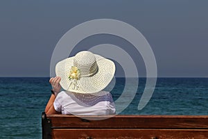 Woman in sun hat sitting on a wooden bench beach on blue sea background