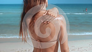 Woman at beach carefully applies sunscreen to shoulder shielding skin from sun damage. Sunscreen fortifies defense