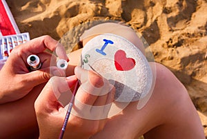 Woman on beach is drawing on pebble - I heart, s