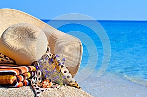 Woman beach hat, bright towel and flowers against blue ocean