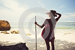 Woman on the beach with hat, stick and backpack