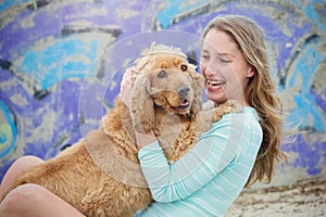 A woman on the beach with her Chocker Spaniel in front of a graffiti wall.