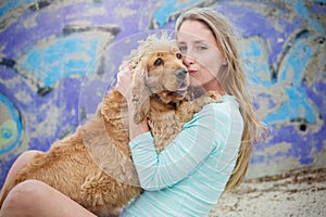 A woman on the beach with her Chocker Spaniel in front of a graffiti wall.