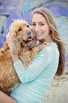 A woman on the beach with her Chocker Spaniel in front of a graffiti wall.