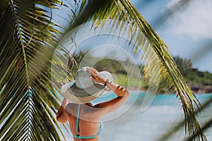 Woman on the beach in the palm trees shadow wearing blue hat. Luxury paradise recreation vacation concept