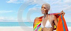 Woman at the beach side wrapped in a colorful towel, African latin American woman enjoying a sunny day with blue sky. Concept of