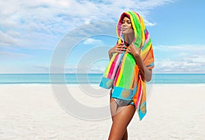 Woman at the beach side wrapped in a colorful towel, African latin American woman enjoying a sunny day with blue sky. Concept of