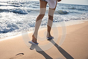 Woman in beach slippers walking on sandy seashore, closeup