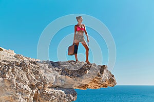 Woman in beachwear with suitcase and glasses. Ocean view from cliff. Time for travel or Summer holiday. Travel desire.