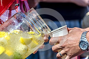 Woman in beads pours cold water with ice and carved lemons from