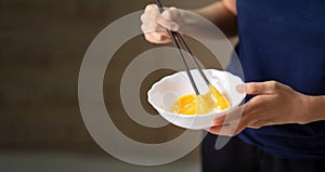 Woman beating eggs with chopsticks closeup