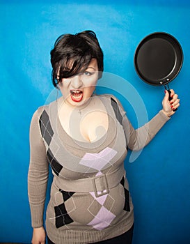 Woman beating with a frying pan on bluw studio background alone