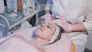 Woman beautician applies cream to woman face.