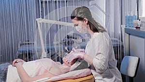 Woman beautician applies cream to woman face.