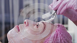 Woman beautician applies a mask to the face of a young woman with a brush.