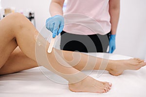 Woman beautician in blue glowes applies contact gel on the leg of a woman for laser hair removal in cosmetology studio