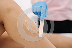 Woman beautician in blue glowes applies contact gel on the leg of a woman for laser hair removal in cosmetology studio