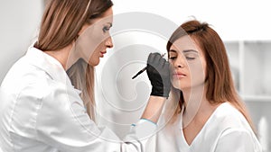 Woman beautician drawing shape improving correcting outline eyebrows to client at beauty salon