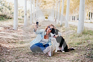 woman and beautiful border collie dog sitting in a path of trees outdoors. woman taking a selfie with mobile phone