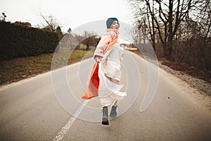 A woman in a beautiful coat and white dress rides along the way. Back viev