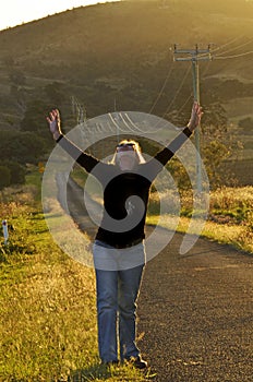 Woman in beautiful countryside raising arms to thank God for answered prayer