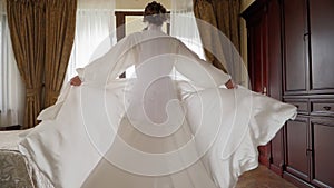 Woman in beautiful developing white robe walks through bedroom to balcony.