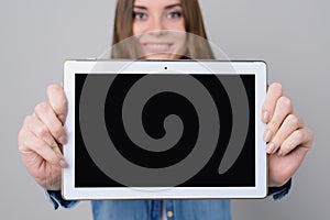 Woman with beautiful face, toothy smile is showing digital tablet with empty black screen. Close up photo, isolated on grey backgr