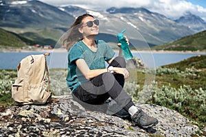 Woman beautiful girl traveler drinking water at a halt. Travel to Norway, beautiful mountain landscape