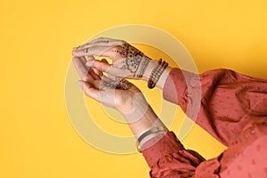 Woman with beautiful henna tattoos on hands against yellow background. Traditional mehndi