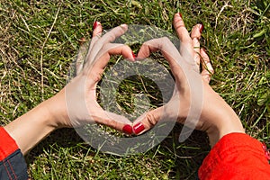 Woman with beautiful manicured hands making the heart sign, on a background of green grass