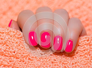 Woman with beautiful manicured pink fingernails gracefully crossing her hands to display them to the viewer on a orange background