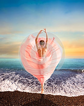 Woman in beautiful pink dress dancing on seacoast