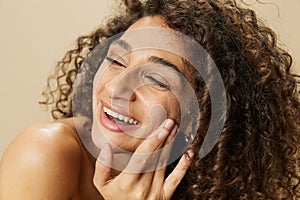 Woman beauty face close-up applying anti-aging moisturizer with fingers of her hand, skin health nails and hair, hair