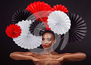 Woman, beauty and hand with origami fans in studio isolated on a dark background. Face, makeup cosmetics and skincare of