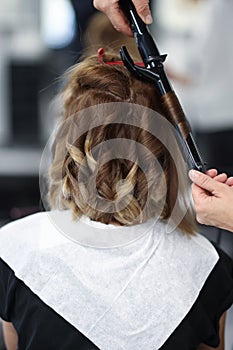 Woman in beauty salon is twisted curls of hair on curling iron.