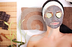 Woman in a beauty salon, wellness. Cosmetic procedure woman`s face in the mask mitigating and cucumber slices on eyes