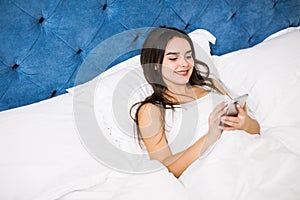 Woman in bed checking social apps with smartphone in the morning at home